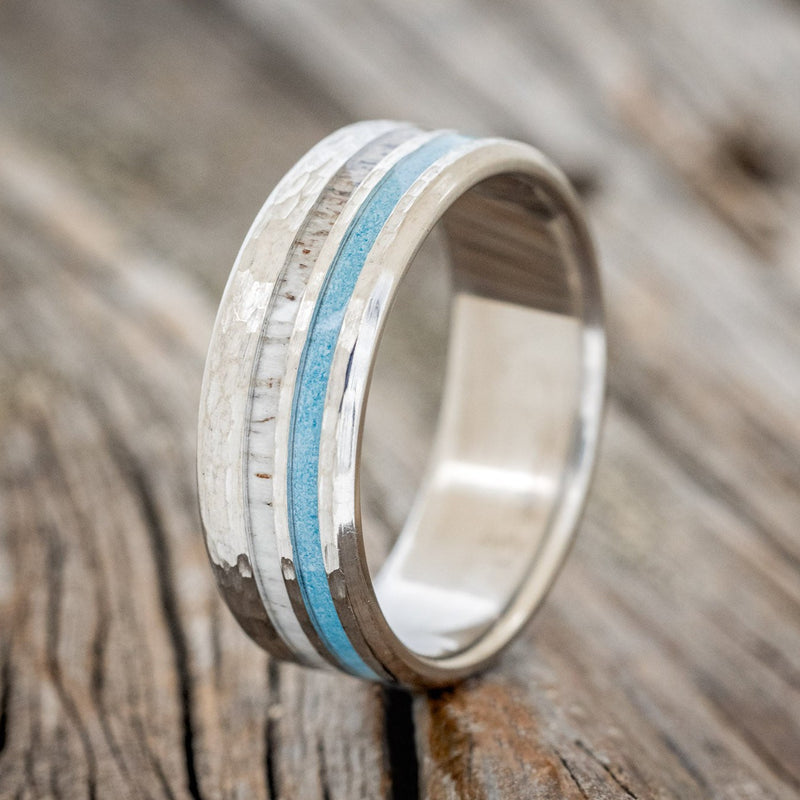Shown here is "Cosmo", a custom, handcrafted men's wedding ring featuring elk antler and hand-crushed turquoise offset into two channels on a hammered band, upright facing left. Additional inlay options are available upon request.