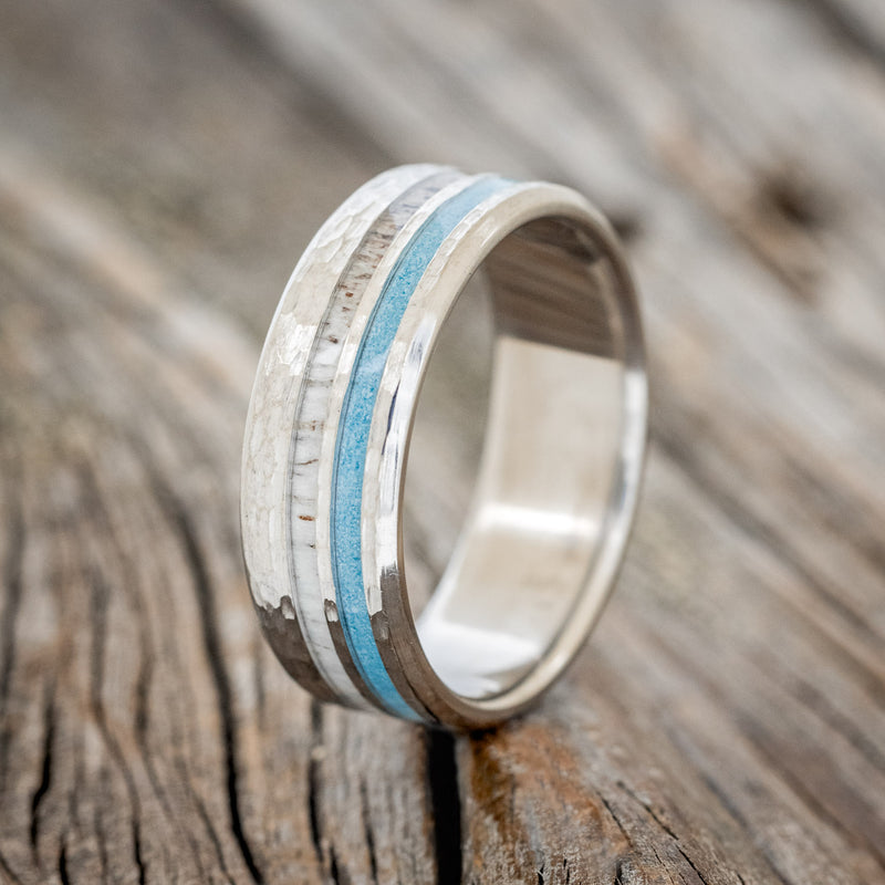 Shown here is "Cosmo", a custom, handcrafted men's wedding ring featuring elk antler and hand-crushed turquoise inlays on a hammered band, upright facing left. 