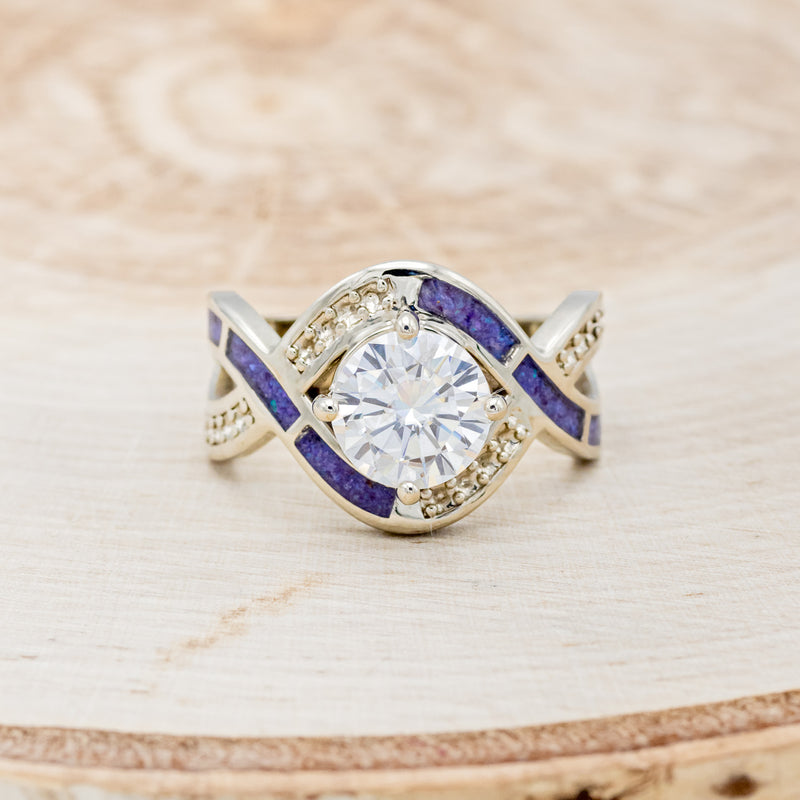 Shown here is "Helix", an infinity-style round cut moissanite women's engagement ring with diamond accents and sleepy lavender opal inlays, front facing. Many other center stone options are available upon request.