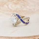 Shown here is "Helix", an infinity-style round cut moissanite women's engagement ring with diamond accents and sleepy lavender opal inlays, facing left. Many other center stone options are available upon request.