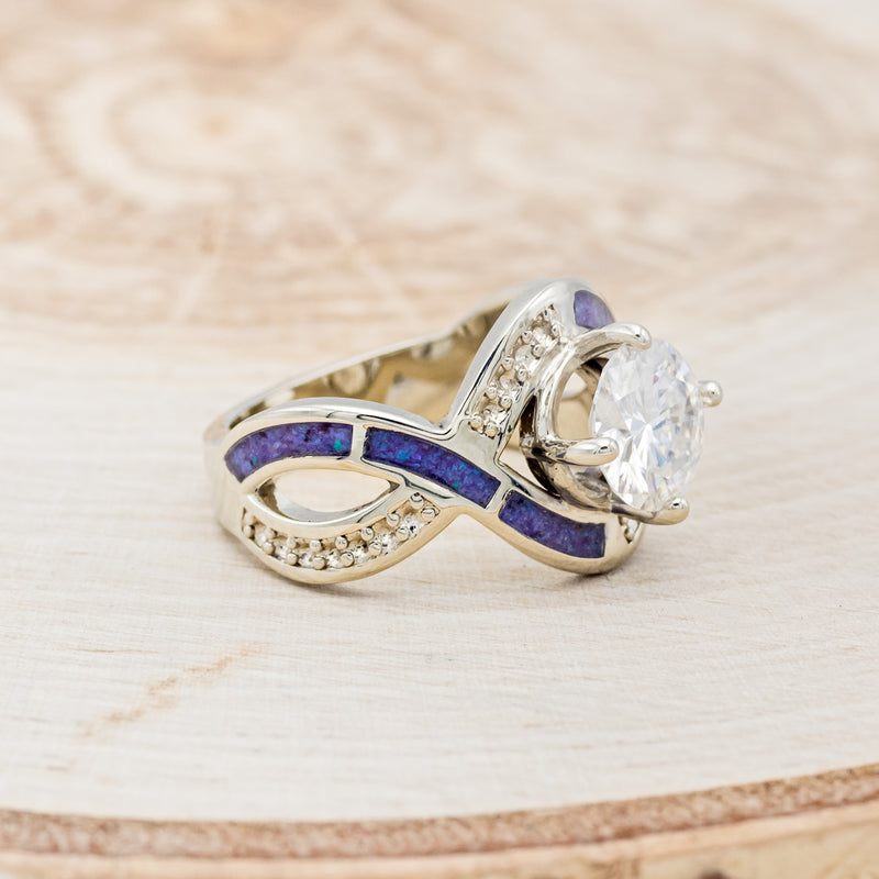 Shown here is "Helix", an infinity-style round cut moissanite women's engagement ring with diamond accents and sleepy lavender opal inlays, facing right. Many other center stone options are available upon request.