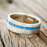 Shown here is "Vertigo", a custom, handcrafted men's wedding ring featuring a blue opal inlay on a hammered band, tilted left. Additional inlay options are available upon request.