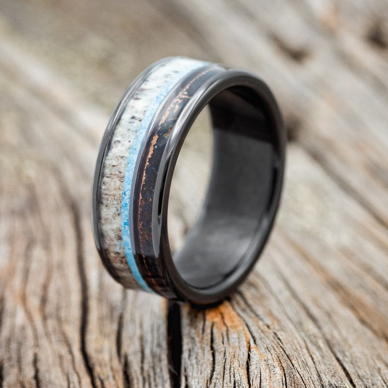 Shown here is "Element", a custom, handcrafted men's wedding ring featuring patina copper, turquoise, and antler inlays, shown here on a fire-treated black zirconium band, upright facing left. Additional inlay options are available upon request.