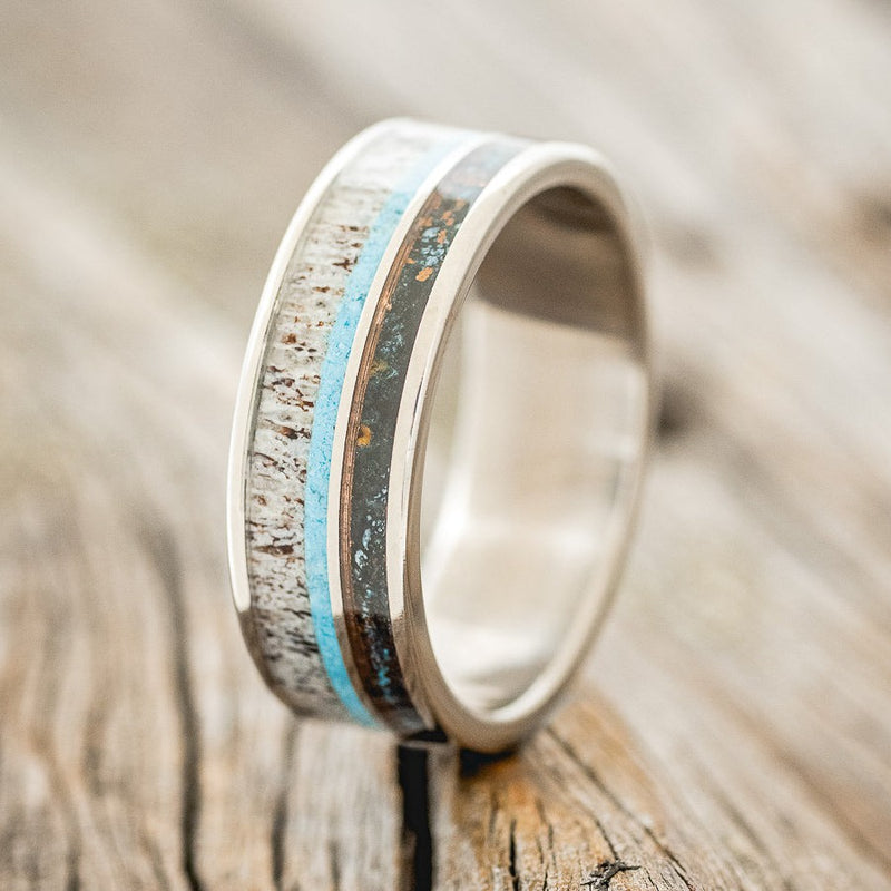 Shown here is "Element", a custom, handcrafted men's wedding ring featuring patina copper, turquoise, and antler inlays, shown here on a titanium band, upright facing left. Additional inlay options are available upon request.