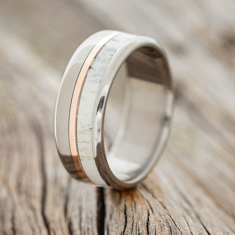 Shown here is "Tanner", a custom, handcrafted men's wedding ring featuring a naturally shed elk antler and a 14K rose gold inlay, upright facing left. Additional inlay options are available upon request.