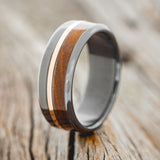Shown here is "Tanner", a custom, handcrafted men's wedding ring featuring ironwood and a 14K rose gold inlay, shown here on a fire-treated black zirconium band, upright facing left. Additional inlay options are available upon request.