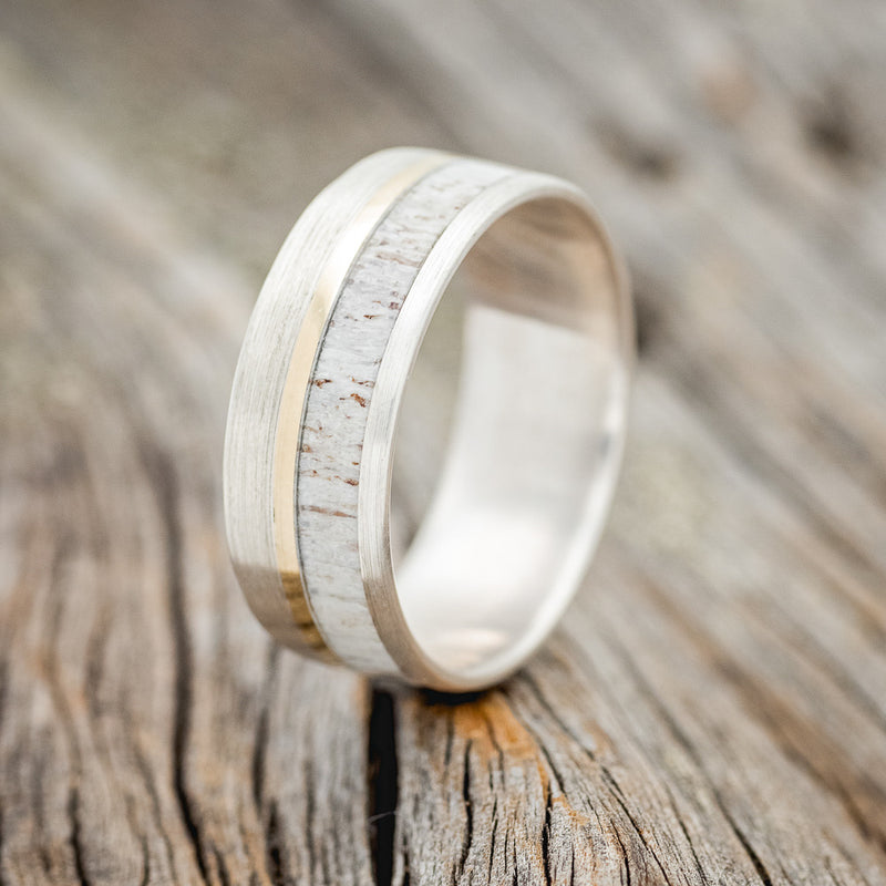 Shown here is "Tanner", a custom, handcrafted brushed men's wedding ring featuring a naturally shed elk antler overlay and a 14K yellow gold inlay, upright facing left. Additional inlay options are available upon request.