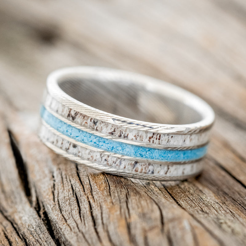 Shown here is "Rio", a custom, handcrafted men's wedding ring featuring 3 channels with antler and turquoise inlays on a titanium band, tilted left. Additional inlay options are available upon request.