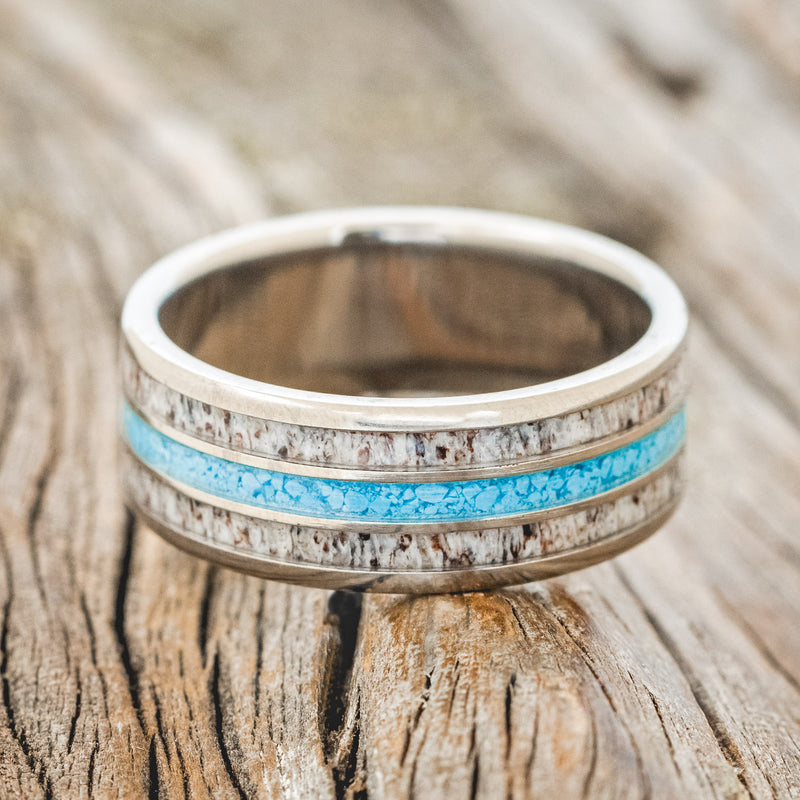 Shown here is "Rio", a custom, handcrafted men's wedding ring featuring 3 channels with antler and turquoise inlays on a titanium band, laying flat. Additional inlay options are available upon request.