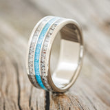Shown here is "Rio", a custom, handcrafted men's wedding ring featuring 3 channels with antler and turquoise inlays on a titanium band, upright facing left. Additional inlay options are available upon request.