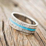 Shown here is "Rio", a custom, handcrafted men's wedding ring featuring 3 channels with antler and turquoise inlays on a titanium band, tilted left. Additional inlay options are available upon request.
