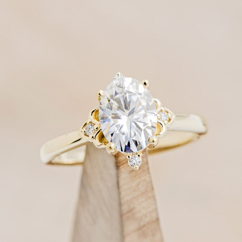 Shown here is "Zella", an oval moissanite women's engagement ring with diamond accents, on stand front facing. Many other center stone options are available upon request. 