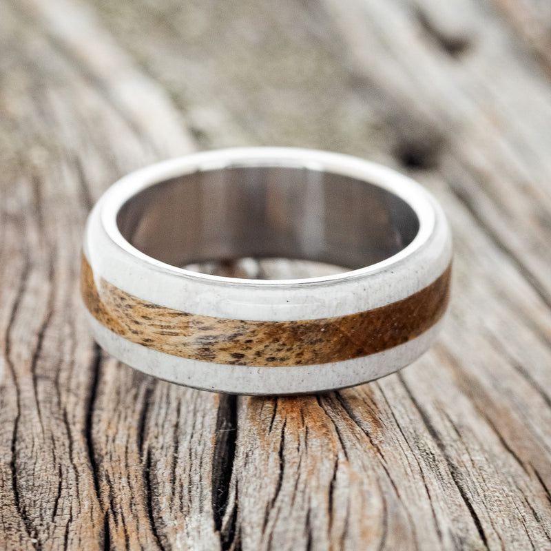 Shown here is "Canyon", a custom, handcrafted men's ring featuring a spalted maple inlay set between two antler overlays, laying flat. Additional inlay options are available upon request.