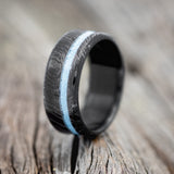 Shown here is "Vertigo", a handcrafted men's wedding ring featuring a turquoise inlay with a woodgrain finish on a fire-treated black zirconium band, upright facing left.