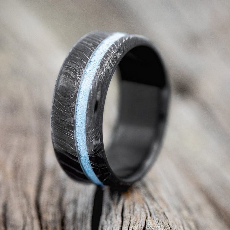 Shown here is "Vertigo" is a custom, handcrafted men's wedding ring featuring a turquoise inlay on a fire-treated black zirconium wedding band with a woodgrain finish, upright facing left. Additional inlay options are available upon request.