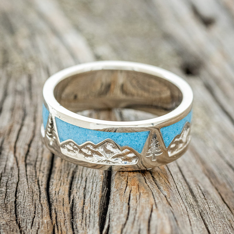 Shown here is "Summit", a custom, handcrafted men's wedding ring featuring a mountain range engraving with turquoise inlays, laying flat. Additional inlay options are available upon request.