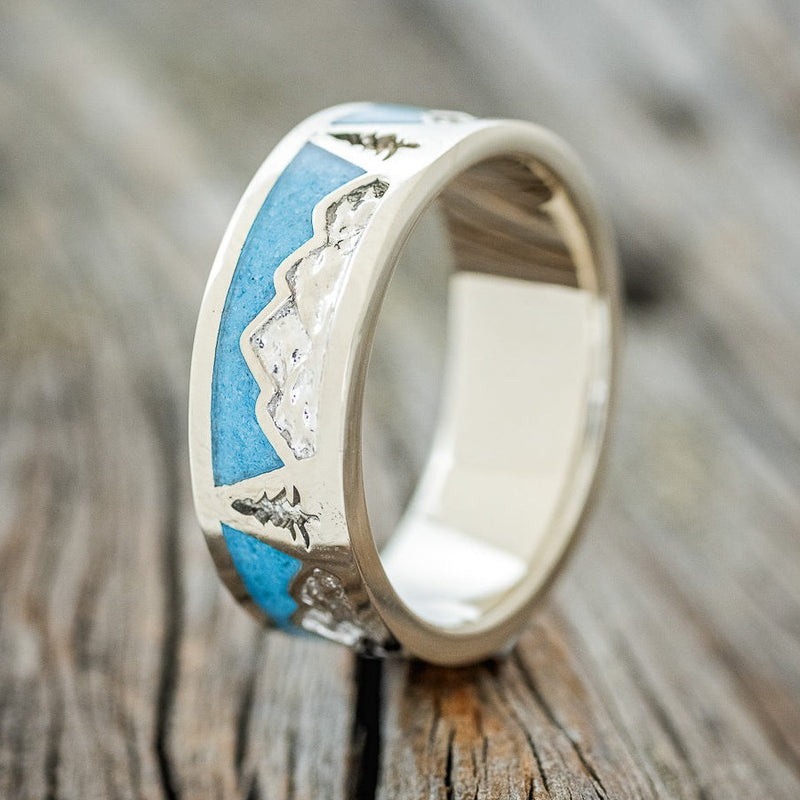 Shown here is "Summit", a custom, handcrafted men's wedding ring featuring a mountain range engraving with turquoise inlays, upright facing left. Additional inlay options are available upon request.