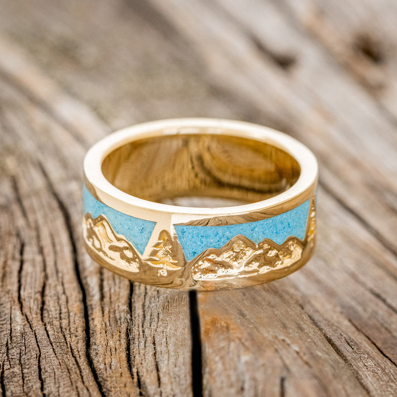 Shown here is "Summit", a custom, handcrafted men's wedding ring featuring a mountain range engraving with turquoise inlays, laying flat. Additional inlay options are available upon request.