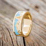 Shown here is "Summit", a custom, handcrafted men's wedding ring featuring a mountain range engraving with turquoise inlays, upright facing left. Additional inlay options are available upon request.