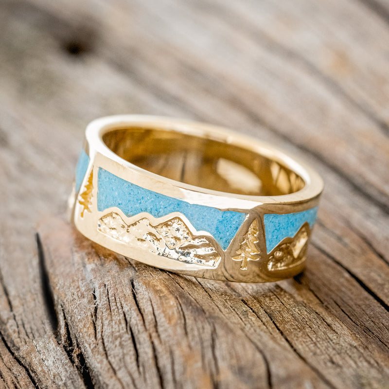 Shown here is "Summit", a custom, handcrafted men's wedding ring featuring a mountain range engraving with turquoise inlays, tilted left. Additional inlay options are available upon request.