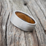 Shown here is "Sedona", a handcrafted whiskey barrel-lined men's wedding ring, featuring a brushed finish, tilted left. Additional inlay options are available upon request.