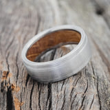 Shown here is "Sedona", a handcrafted whiskey barrel-lined men's wedding ring, featuring a brushed finish, tilted right. Additional inlay options are available upon request.