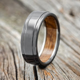 Shown here is "Sedona", a custom, handcrafted men's wedding ring featuring a raised center with a whiskey barrel oak lining on a fire-treated black zirconium band, upright facing left. Additional lining options are available upon request.