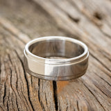 Shown here is "Sedona", a custom, handcrafted men's wedding ring featuring a solid metal band with a raised center, laying flat. Additional inlay options are available upon request.