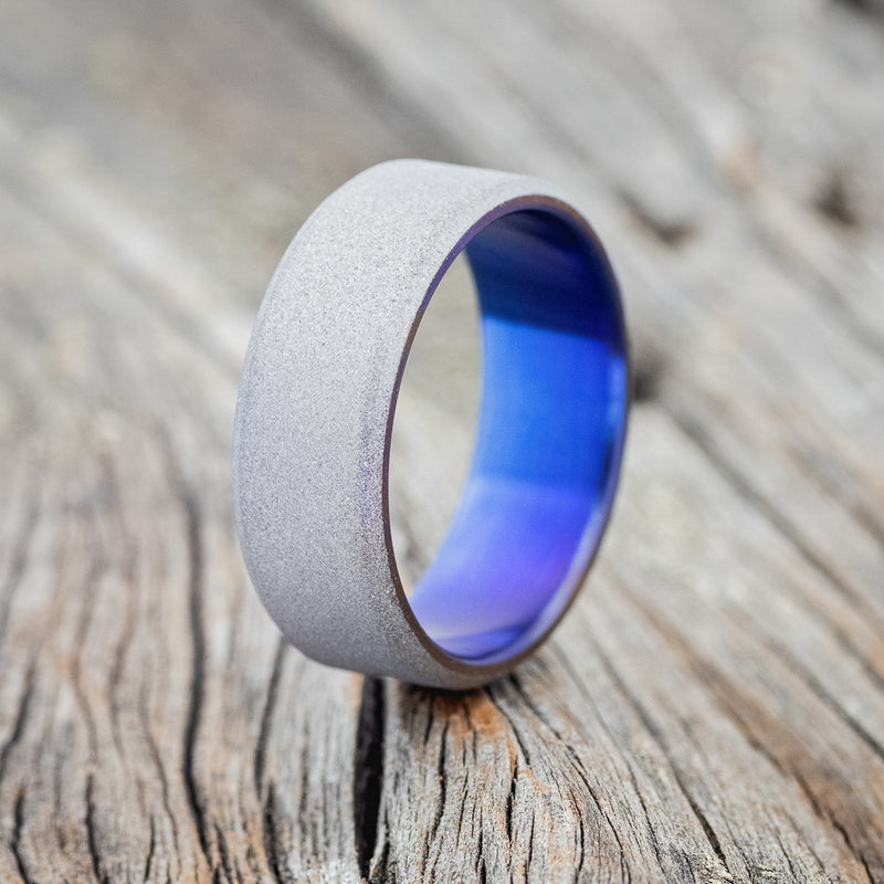 Shown here is a handcrafted men's wedding ring featuring a titanium band with a sandblasted finish and fire-treated lining, upright facing left. Please note the color of the fire-treated lining can vary. Additional inlay options are available upon request.