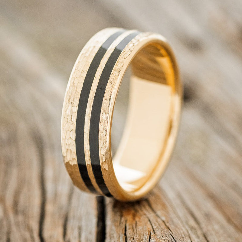 Shown here is "Cosmo", a custom, handcrafted men's wedding ring featuring a 14K gold base with two black acrylic inlays and a hammered finish, upright facing left. Additional inlay options are available upon request.