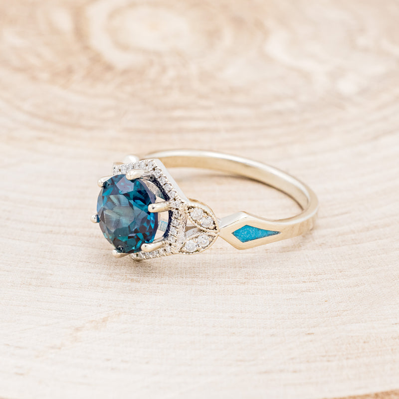 Shown here is "Lucy in the Sky", a halo-style lab-created alexandrite women's engagement ring with diamond accents and turquoise inlays, facing left. Many other center stone options are available upon request.