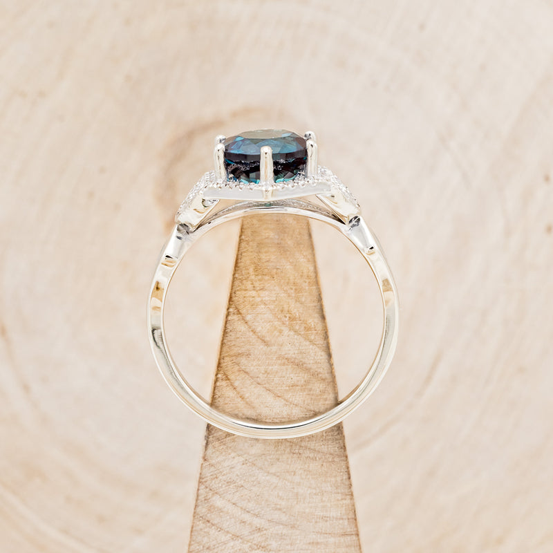 Shown here is "Lucy in the Sky", a halo-style lab-created alexandrite women's engagement ring with diamond accents and turquoise inlays, side view on stand. Many other center stone options are available upon request.