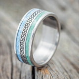Shown here is "Ryder", a custom engraved Celtic sailor's knot-patterned men's wedding ring featuring malachite and turquoise inlays, upright facing left. Additional inlay options are available upon request.