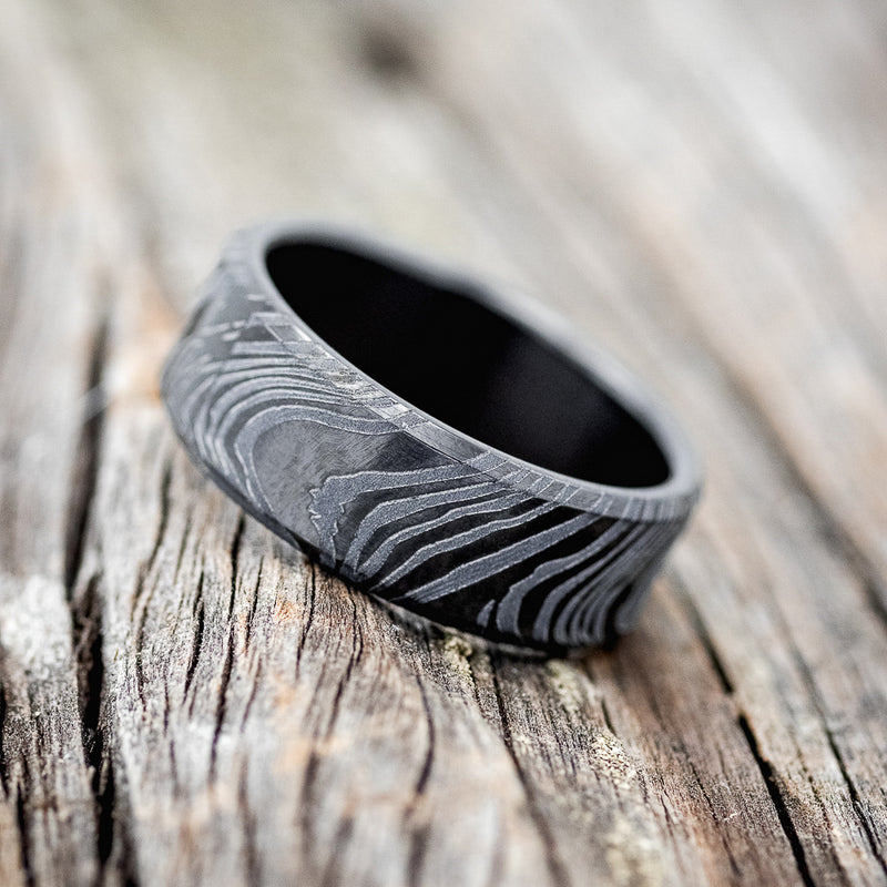 Shown here is a handcrafted men's wedding ring shown featuring a solid band with a woodgrain pattern finish, tilted left.