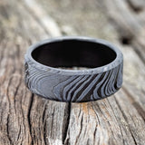 Shown here is a handcrafted men's wedding ring featuring a solid band with a woodgrain pattern, laying flat. Additional inlay options are available upon request.