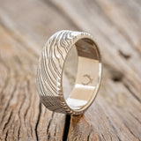 Shown here is a handcrafted men's wedding ring shown featuring a solid band with a woodgrain pattern finish, upright facing left.