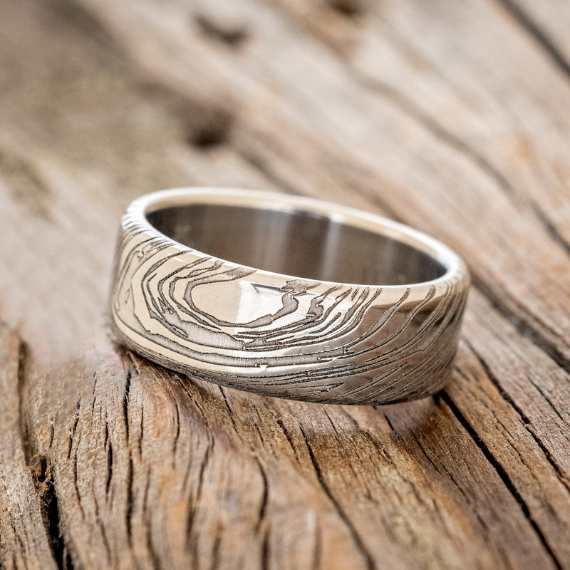 Shown here is a handcrafted men's wedding ring shown featuring a solid band with a woodgrain pattern finish, tilted left.