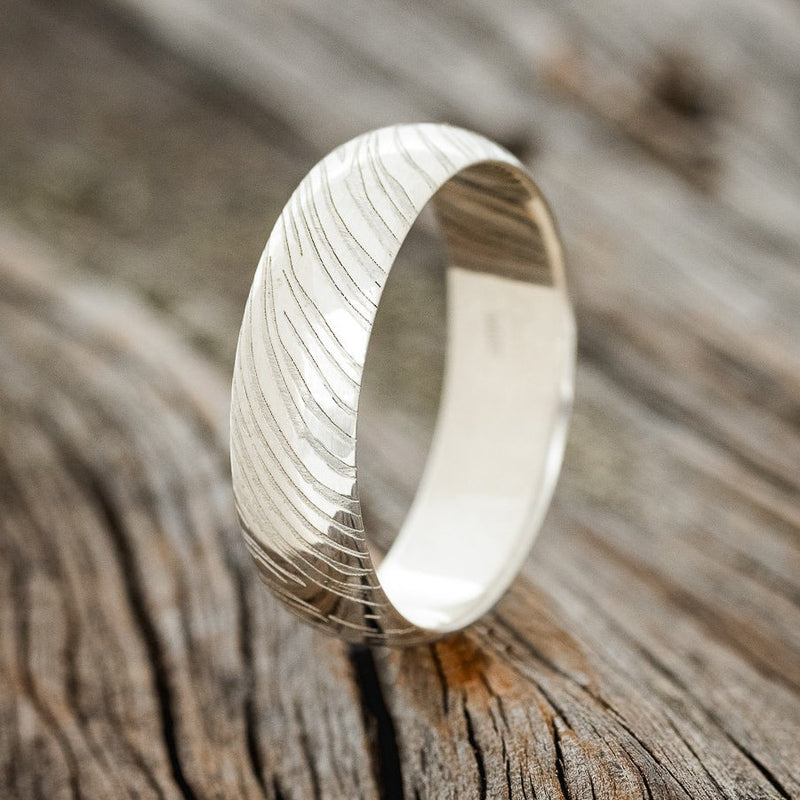 Shown here is a handcrafted men's wedding ring featuring a domed band with a custom woodgrain pattern engraving, upright facing left. Additional engraving options are available upon request.