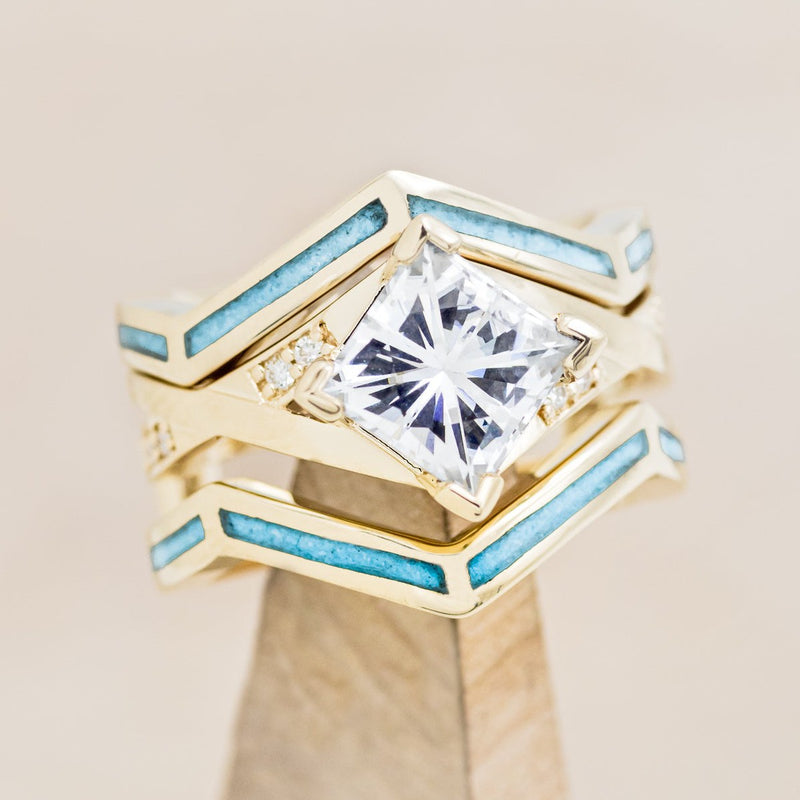 Shown here is "Lina", a moissanite women's engagement ring with diamond accents and a turquoise ring guard, on stand front facing. Many other center stone options are available upon request.