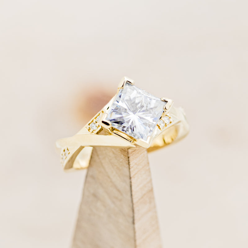 Shown here is "Lina", a moissanite women's engagement ring with diamond accents, on stand facing slightly right. Many other center stone options are available upon request.