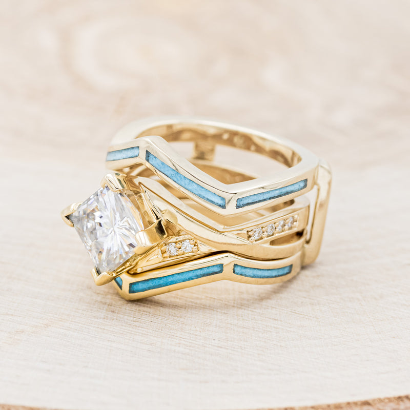 Shown here is "Lina", a moissanite women's engagement ring with diamond accents and a turquoise ring guard, facing left. Many other center stone options are available upon request.