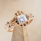 Shown here is "Eileen", a vintage-style moissanite women's engagement ring with black diamond accents and tracer, on stand tilted right. Many other center stone options are available upon request. 
