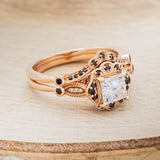 Shown here is "Eileen", a vintage-style moissanite women's engagement ring with black diamond accents and tracer, facing right. Many other center stone options are available upon request.