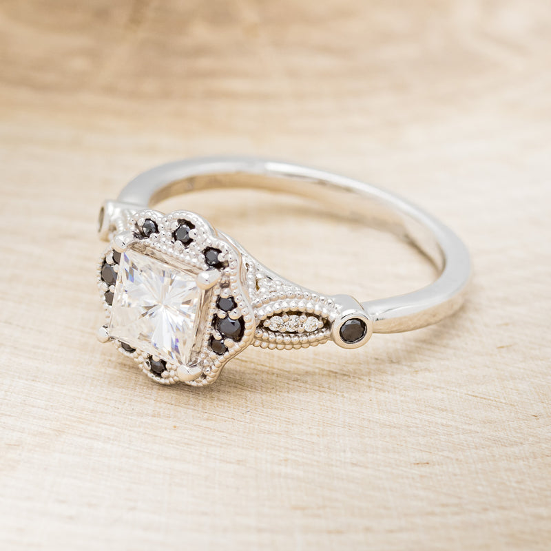Shown here is "Eileen", a vintage-style moissanite women's engagement ring with black diamond accents, facing left. Many other center stone options are available upon request.