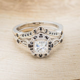 Shown here is "Eileen", a vintage-style moissanite women's engagement ring with black diamond accents and tracer, front facing. Many other center stone options are available upon request.