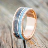Shown here is "Raptor", a custom, handcrafted men's wedding ring featuring 2 channels with turquoise and patina copper inlays on a hammered 14K gold band, upright facing left. Additional inlay options are available upon request.