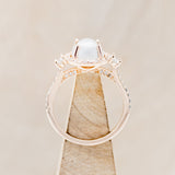 Shown here is "KB", an oval white buffalo turquoise women's engagement ring with a diamond halo and diamond accents, side view on stand. Many other center stone options are available upon request.