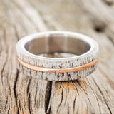 Shown here is "Golden", a handcrafted men's wedding ring featuring a naturally shed elk antler divided by a 14K rose gold inlay, laying flat. Additional inlay options are available upon request.