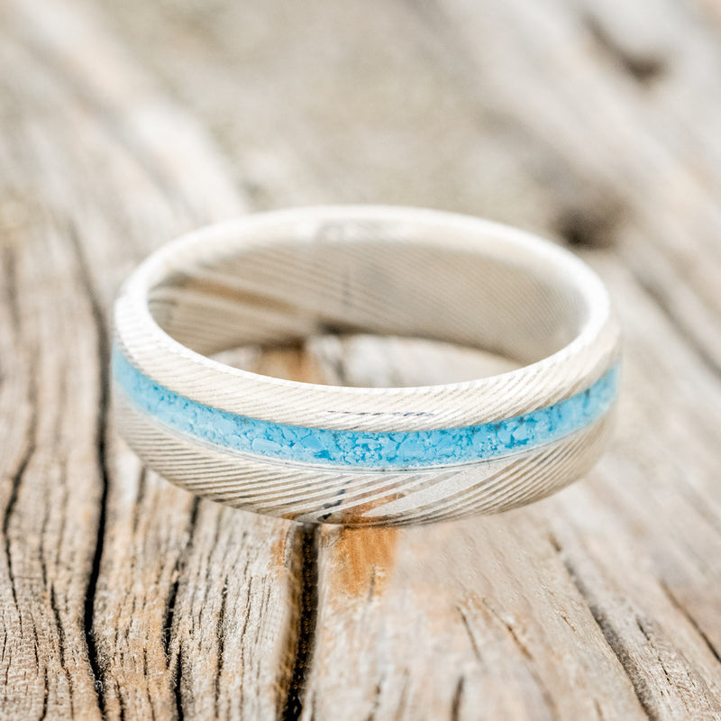 Shown here is "Vertigo", a handcrafted men's narrow wedding ring featuring a turquoise inlay, laying flat.