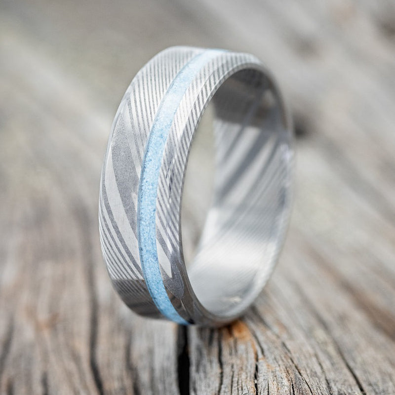 Shown here is "Vertigo", a custom, handcrafted men's wedding ring featuring a turquoise inlay, shown here in a Damascus steel band, upright facing left. Additional inlay options are available upon request.